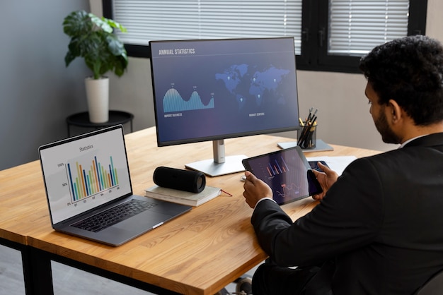 Business professional analyzing real-time network statistics on a tablet, laptop, and desktop monitor, showcasing cybersecurity traffic analysis tools.